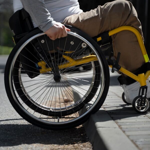 Imagem de pessoa em cadeira de rodas em uma calçada, que não segue as normas de acessibilidade da ABNT.