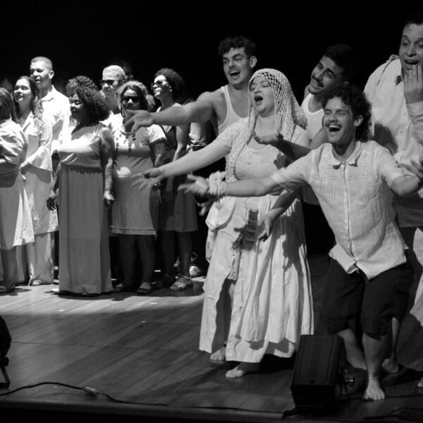 Foto em preto e branco da Orquestra Brasileira de Cantores Cegos, que estreia no Sesc, durante ensaio com a Cia Poéticas Contemporânea. São pessoas de diferentes idades, gênero e raça, com deficiência visual.