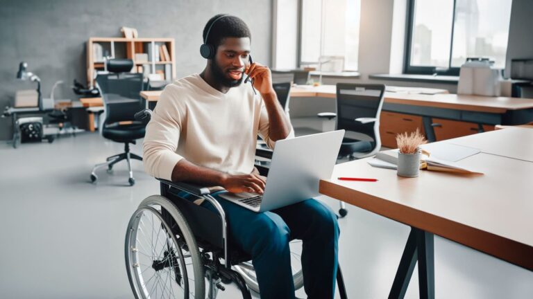 Homem negro em cadeira de rodas, trabalhando com um laptop no escritório. Imagem ilustra as 9 vagas de níveis júnior a sênior para profissionais com deficiência.