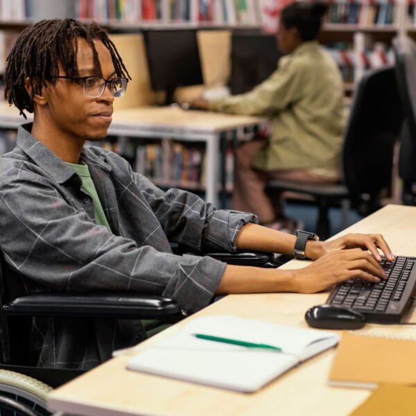 Pessoa em cadeira de rodas usando um computador em uma biblioteca. Programa Desenvolve 2024.