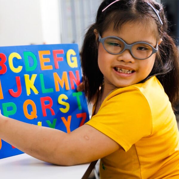 Criança segurando um livro didático com o alfabeto, retratando a educação inclusiva na escola regular.