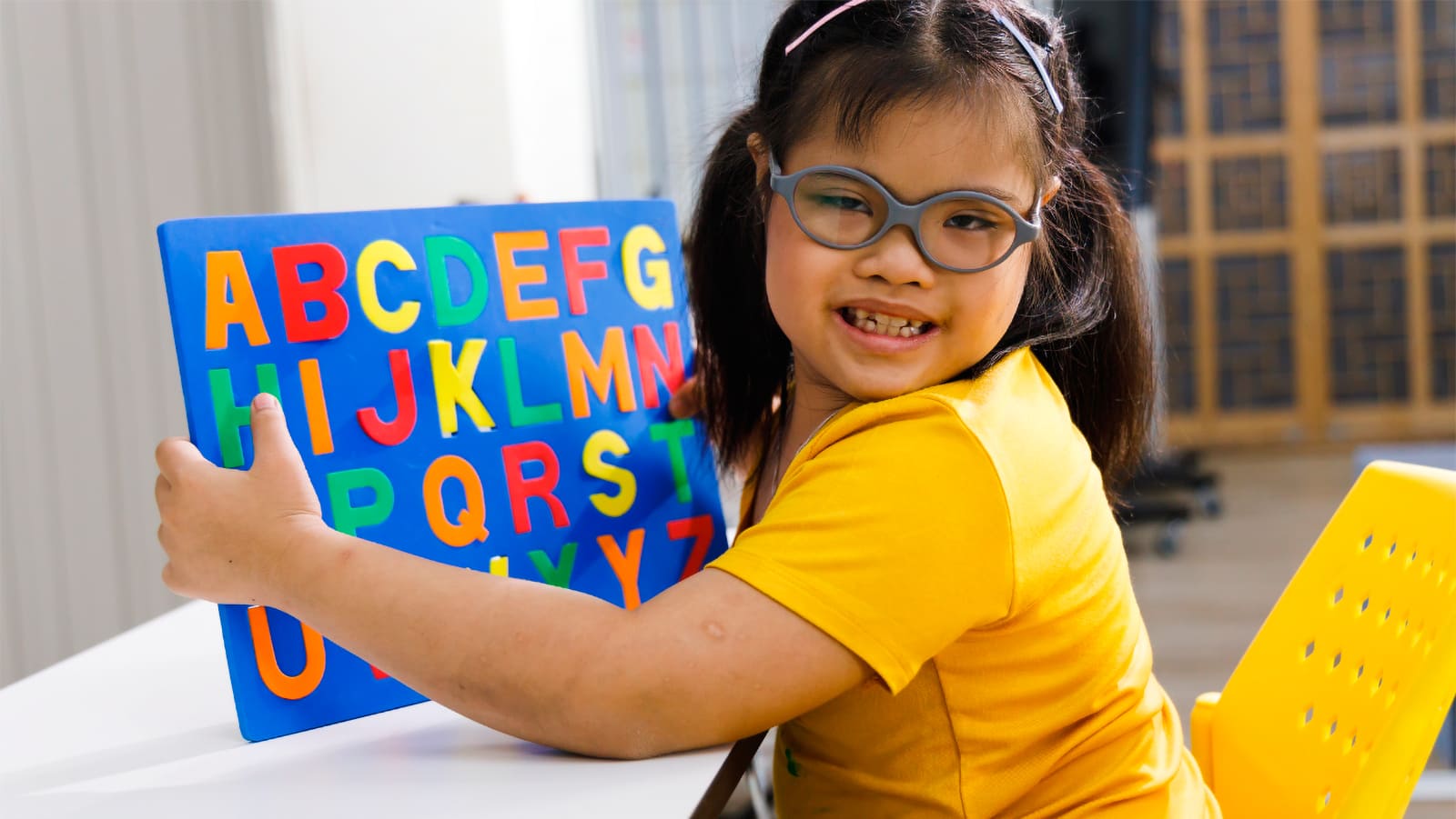 Criança segurando um livro didático com o alfabeto, retratando a educação inclusiva na escola regular.