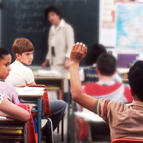 Sociedade e burocracia: Estudantes em uma sala de aula, com o professor ao fundo. Um aluno está com a mão levantada e outros o olhando, retratando a dificuldade em ser um cidadão com deficiência.
