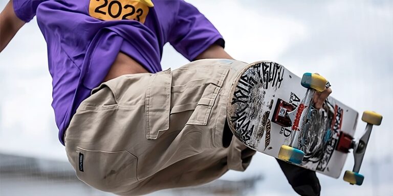 Paraskatista em ação, usando camiseta roxa e calças cáqui, realizando manobra com o skate, presente no Sesc Verão 2024, inspirado nos Jogos Olímpicos e Paralímpicos de Paris.