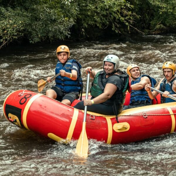 Um grupo de pessoas praticando rafting em um rio de corredeiras, durante edição do Camping Acessível.