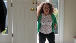 Pessoa entrando por uma porta aberta, iluminada por luz natural; cena do documentário sobre Natalia Grace, que tem displasia espondiloepifisária.
