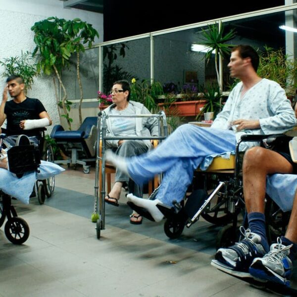 Pessoas com deficiência aguardando em uma área externa, incluindo quatro pessoas em cadeiras de rodas e uma pessoa com um andador.