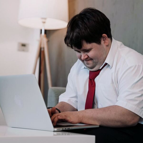 Profissional concentrado no trabalho, usando um laptop e sorrindo. Ilustra as 15 vagas de emprego para profissionais com deficiência.