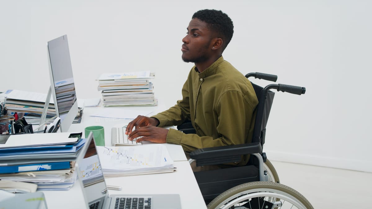 Profissional em cadeira de rodas engajado no trabalho de escritório, ilustrando as 10 vagas de emprego e inclusão no ambiente profissional.