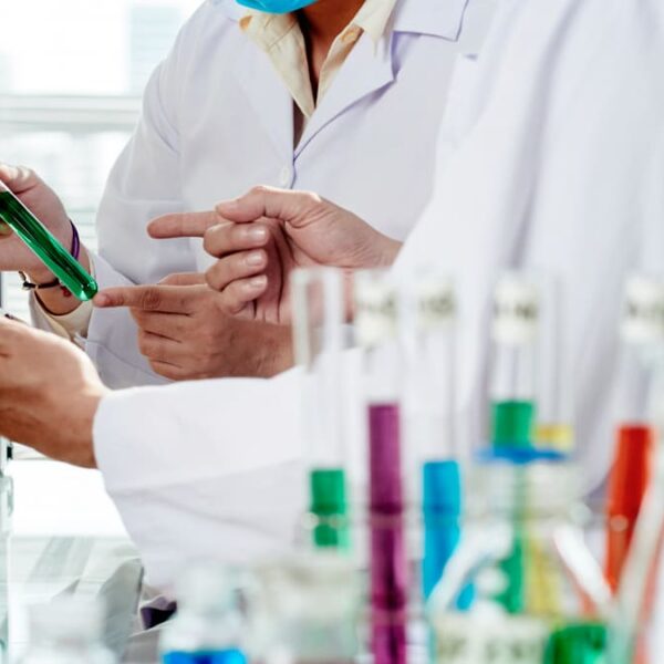 Dois cientistas vestidos com jalecos brancos, conduzindo pesquisa clínica em um laboratório, com um microscópio e tubos de ensaio coloridos no fundo.