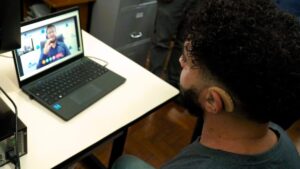 Homem com aparelho auditivo participa de videochamada em um laptop, enquanto é atendido pela central de Libras no Poupatempo.