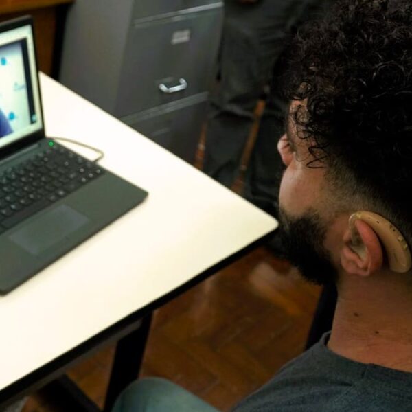 Homem com aparelho auditivo participa de videochamada em um laptop, enquanto é atendido pela central de Libras no Poupatempo.