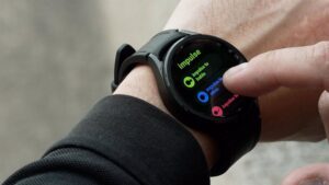 Relógio inteligente com a tela exibindo o app da Samsung para pessoas gagas, com o nome Impulse, e um dedo interagindo com a tela.