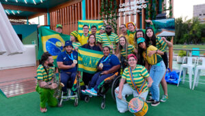 Grupo de pessoas, incluindo musicistas e atletas em cadeiras de rodas, posando com bandeiras do Brasil, na primeira Casa Brasil Paralímpico em Santiago 2023.