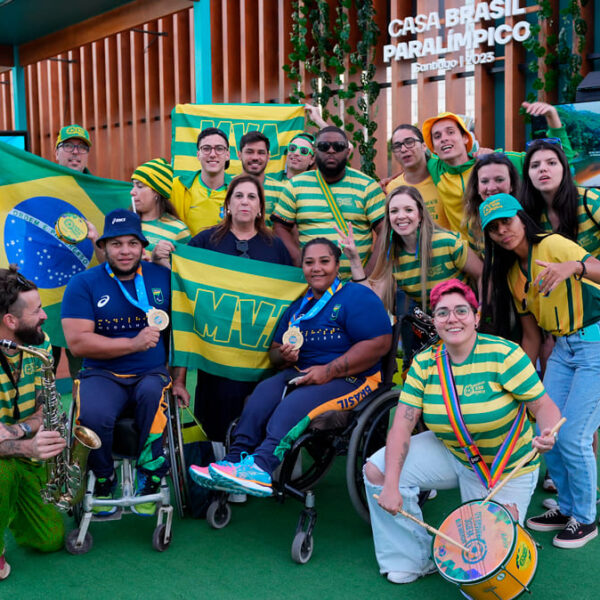 Grupo de pessoas, incluindo musicistas e atletas em cadeiras de rodas, posando com bandeiras do Brasil, na primeira Casa Brasil Paralímpico em Santiago 2023.