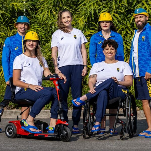 Seis atletas da delegação brasileira, incluindo quatro mulheres e dois homens, posam ao ar livre, usando uniforme oficial e sandálias Havaianas inclusivas.