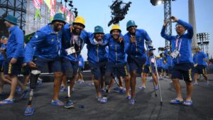 Atletas do Brasil, usando uniformes azuis com "Brasil" escrito, sorriem e em grupo na Abertura da Paralimpíada de Paris 2024. Alguns utilizam próteses ou muletas, todos usando chinelos e chapéus coloridos, comemorando durante o evento esportivo.