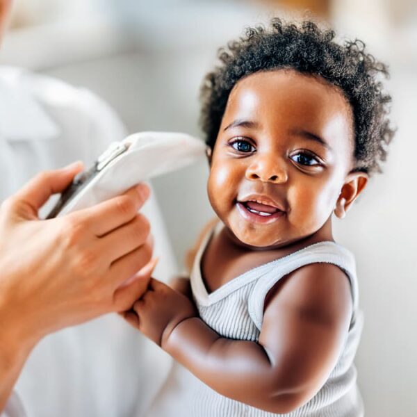 Bebê sorrindo enquanto profissional de saúde realiza a triagem auditiva neonatal, também conhecida como teste da orelhinha.