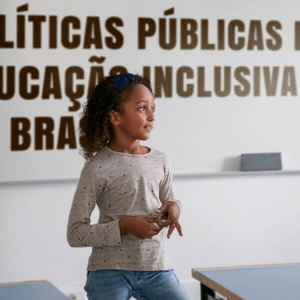 Menina apresentando em sala de aula com o texto "Políticas públicas para educação inclusiva no Brasil" no quadro.