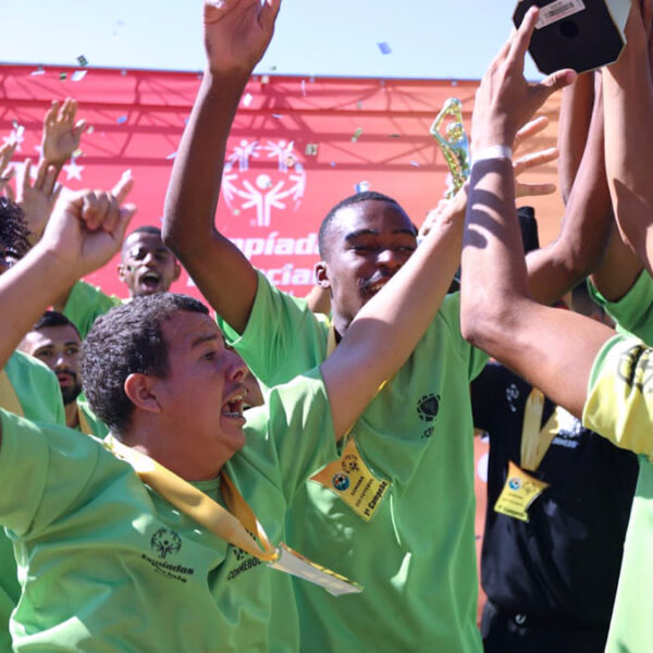 Atletas da delegação brasileira comemoram a vitória, levantando um troféu. A equipe, que irá aos Jogos Latino-Americanos das Olimpíadas Especiais 2024, veste camisetas verdes e medalhas douradas.