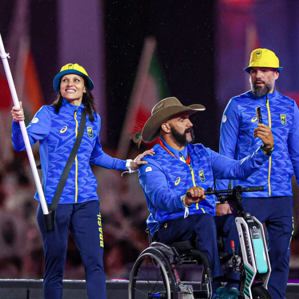 Carol Santiago e Fernando Rufino na cerimônia de encerramento dos Jogos Paralímpicos de Paris 2024, consagrando o Brasil como potência paralímpica. Carol segura a bandeira brasileira e sorri, enquanto Fernando está em cadeira de rodas usando um chapéu de cowboy.