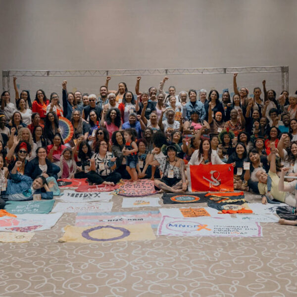 Grupo diverso de mulheres e apoiadoras posam juntas para uma foto em um salão durante o "Encontro Diálogo Mulheres em Movimento 2024", promovido pelo ELAS+.