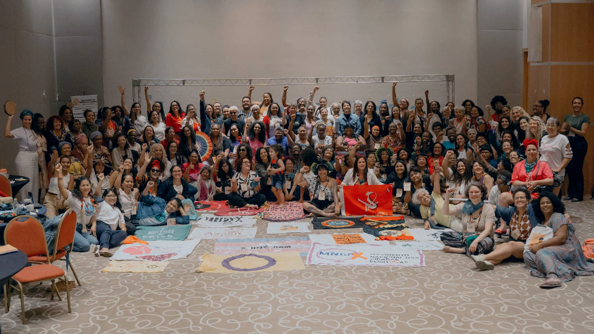 Grupo diverso de mulheres e apoiadoras posam juntas para uma foto em um salão durante o "Encontro Diálogo Mulheres em Movimento 2024", promovido pelo ELAS+.