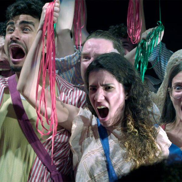 Integrantes da Orquestra Brasileira de Cantores Cegos em cena teatral, expressando emoção com fitas coloridas nas mãos.