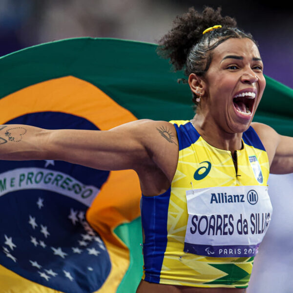 Rayane Soares da Silva comemora emocionada com a bandeira do Brasil após vitória, vestindo uniforme amarelo e azul, garantindo o país no top 5 Paralímpico.