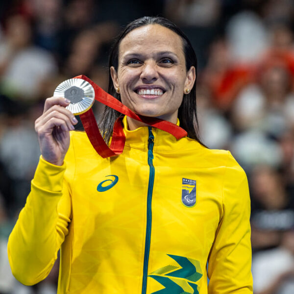 Maria Carolina Santiago, nadadora paralímpica brasileira, sorri e exibe medalha de prata na Paralimpíada de Paris 2024, vestindo uniforme amarelo do Time Brasil.