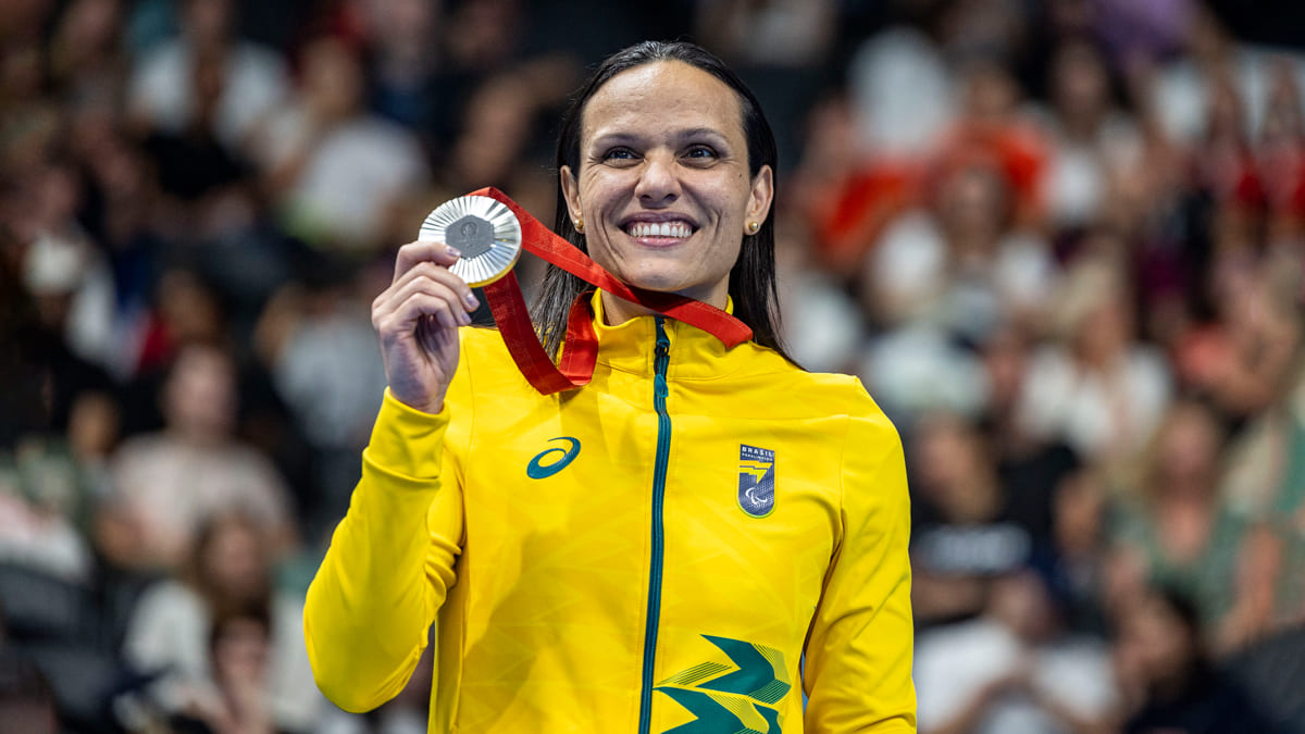 Maria Carolina Santiago, nadadora paralímpica brasileira, sorri e exibe medalha de prata na Paralimpíada de Paris 2024, vestindo uniforme amarelo do Time Brasil.