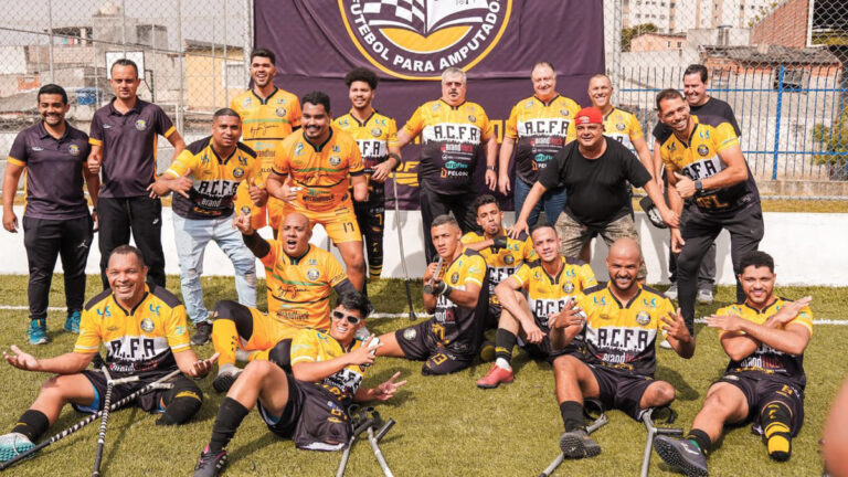 A equipe do Acre Clube de futebol de amputados, favorita da Série B do Brasileirão, posando para foto em um campo, com uniformes amarelos e pretos. Alguns estão sentados e sorrindo, segurando muletas.