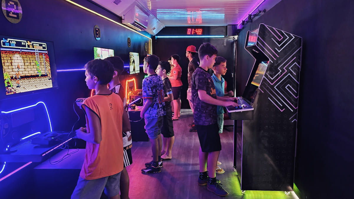 Crianças jogando em videogames e fliperamas em uma exposição de jogos eletrônicos na carreta Cine Geek Game.