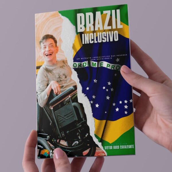 Mãos segurando o livro intitulado "Brazil Inclusivo", com a imagem de um jovem sorridente em cadeira de rodas sobre um fundo que mistura a bandeira do Brasil.