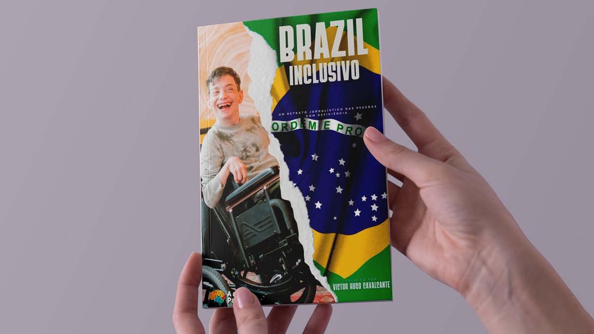 Mãos segurando o livro intitulado "Brazil Inclusivo", com a imagem de um jovem sorridente em cadeira de rodas sobre um fundo que mistura a bandeira do Brasil.