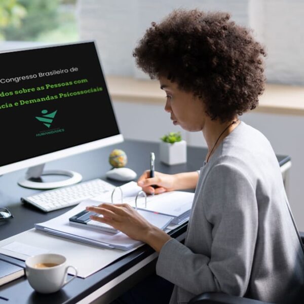 Mulher negra em cadeira de rodas, escrevendo em um caderno enquanto olha para a tela do computador, que exibe informações do "2º Congresso Brasileiro de Estudos sobre Pessoas com Deficiência e Demandas Psicossociais".