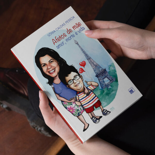 Mãos seguram o livro "Afetos de mãe: amor, morte e vida", com capa ilustrada mostrando uma mulher e uma criança - Sônia e Pedro - em frente à Torre Eiffel.