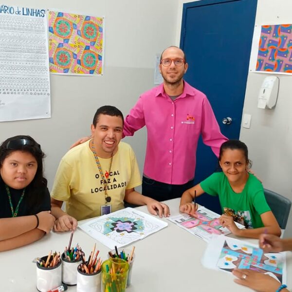 Ricardo Valverde, supervisor do serviço de Longevidade do Instituto Jô Clemente, com grupo de pessoas participando de uma oficina de arte, com desenhos coloridos sobre a mesa. (Foto: Reprodução)