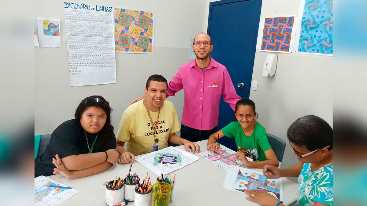 Ricardo Valverde, supervisor do serviço de Longevidade do Instituto Jô Clemente, com grupo de pessoas participando de uma oficina de arte, com desenhos coloridos sobre a mesa. (Foto: Reprodução)