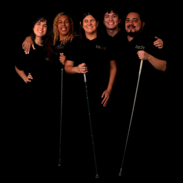 Cinco pessoas que integram o grupo Teatro Cego, três delas segurando bengalas, posam sorrindo em fundo preto. (Foto: Iasmin Dib)