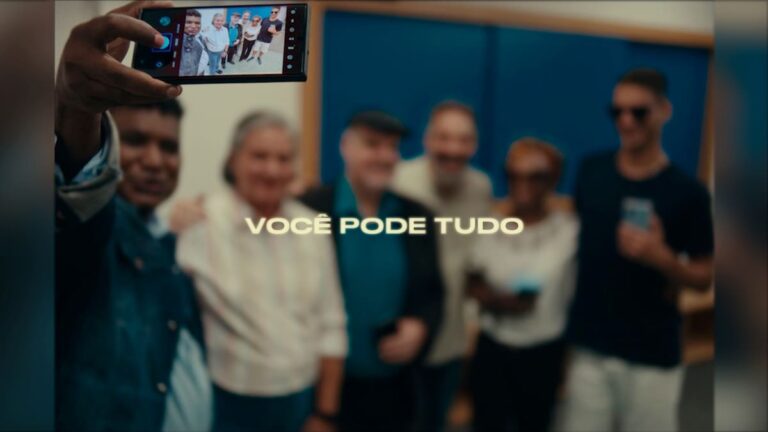 O fotógrafo cego João Maia segura o celular para tirar uma selfie com um grupo diverso, acompanhado da frase "Você pode tudo" ao centro da imagem. (Foto: Reprodução)