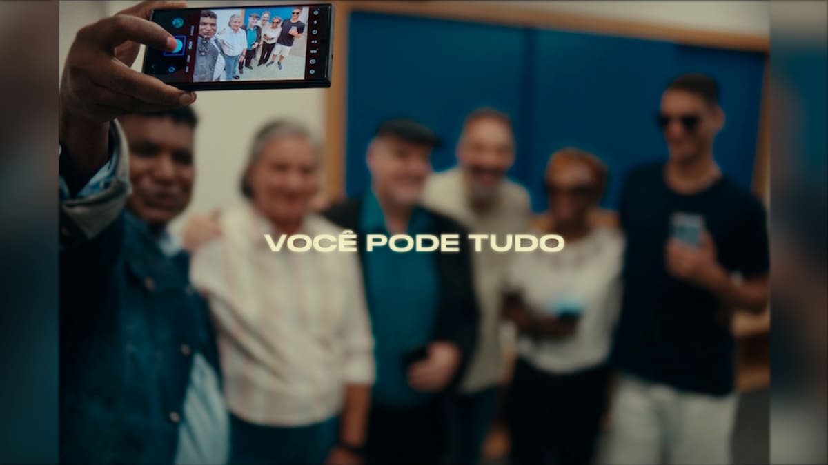 O fotógrafo cego João Maia segura o celular para tirar uma selfie com um grupo diverso, acompanhado da frase "Você pode tudo" ao centro da imagem. (Foto: Reprodução)
