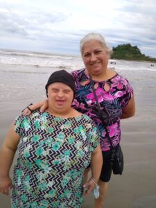Rita com a filha Ana Paula sorrindo na beira do mar com roupas coloridas.