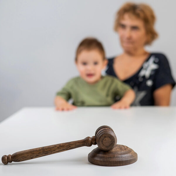 Martelo de juiz sobre mesa com mãe e criança ao fundo, simbolizando decisão judicial relacionada à família e redução da jornada de trabalho. (Créditos: Depositphotos)
