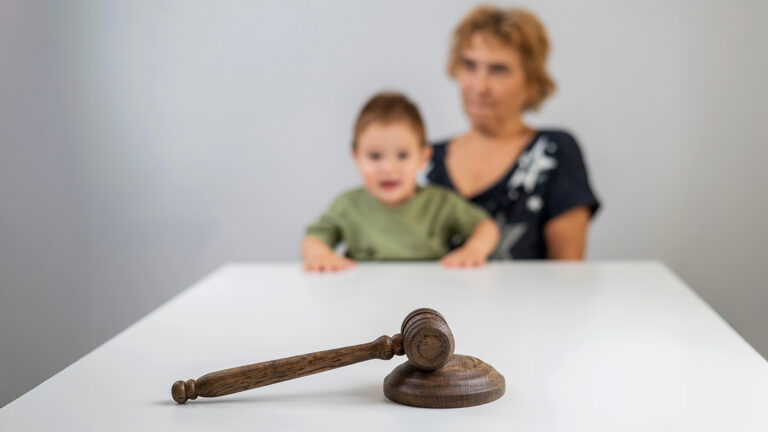 Martelo de juiz sobre mesa com mãe e criança ao fundo, simbolizando decisão judicial relacionada à família e redução da jornada de trabalho. (Créditos: Depositphotos)