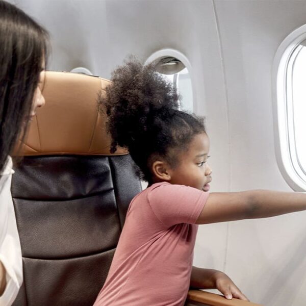 Menina curiosa apontando para fora da janela de um avião enquanto uma mulher a observa. (Créditos: Depositphotos)
