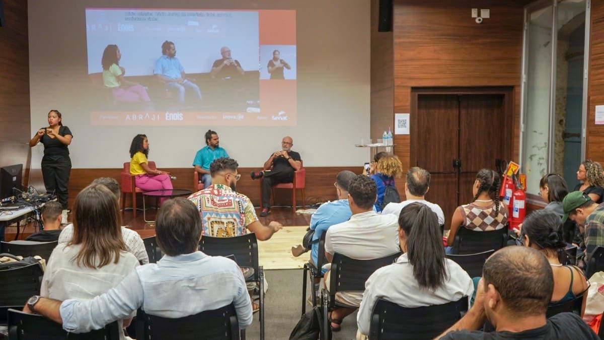 Roda de conversa no Congresso Inova.aê, com três palestrantes no palco e intérprete de Libras ao lado. O público acompanha a atividade em auditório, com projeção ao fundo ampliando a visualização do evento. (Foto: Divulgação)