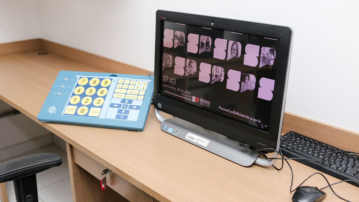 Estação de trabalho com computador e teclado acessível de teclas grandes, voltado para pessoas com deficiência, exibindo na tela o portal PessoaComDeficiencia.sp.gov.br, na Escola da Inclusão. (Foto: Acervo Univesp)