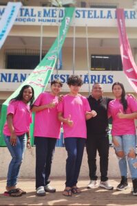 Equipe de estudantes paraenses do app My Tea posa com educador em frente a escola, vestindo camisetas rosa do grupo NORTACK.
