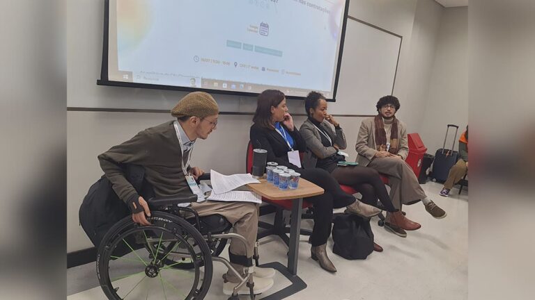 Painel no Congresso da Abraji 2025, com quatro pessoas jornalistas – incluindo uma em cadeira de rodas – sentadas em frente a uma tela de projeção. (Foto: Luiz Guilherme Lima)
